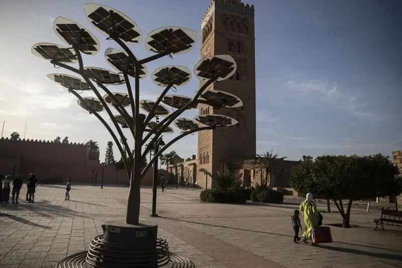 People walk past a solar tree that generates energy using panels, in front of the landmark Kotoubia mosque in Marrakech, November 2022